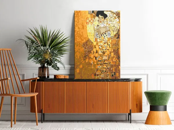 Zeitgenössischer Wohnraum mit Gustav Klimts „Porträt von Adele Bloch-Bauer“ auf einem Sideboard, umgeben von Grün und stilvollen Möbeln.
