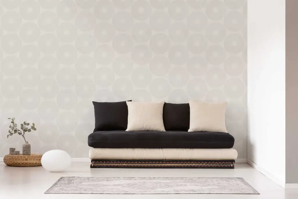 Minimalistisches Wohnzimmer mit beigem Sofa, schwarzen Kissen und schlichter Wandgestaltung in hellen Farben