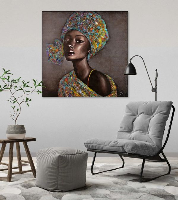 Large square canvas art featuring a Black woman in a colorful, textured headwrap and garment, styled above a grey lounge chair in a minimalist living room.